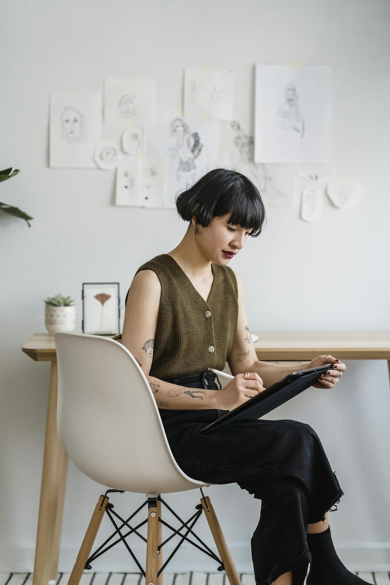 A young woman artist sketching on a tablet in a modern office setting, surrounded by artwork. Creative and focused atmosphere.
