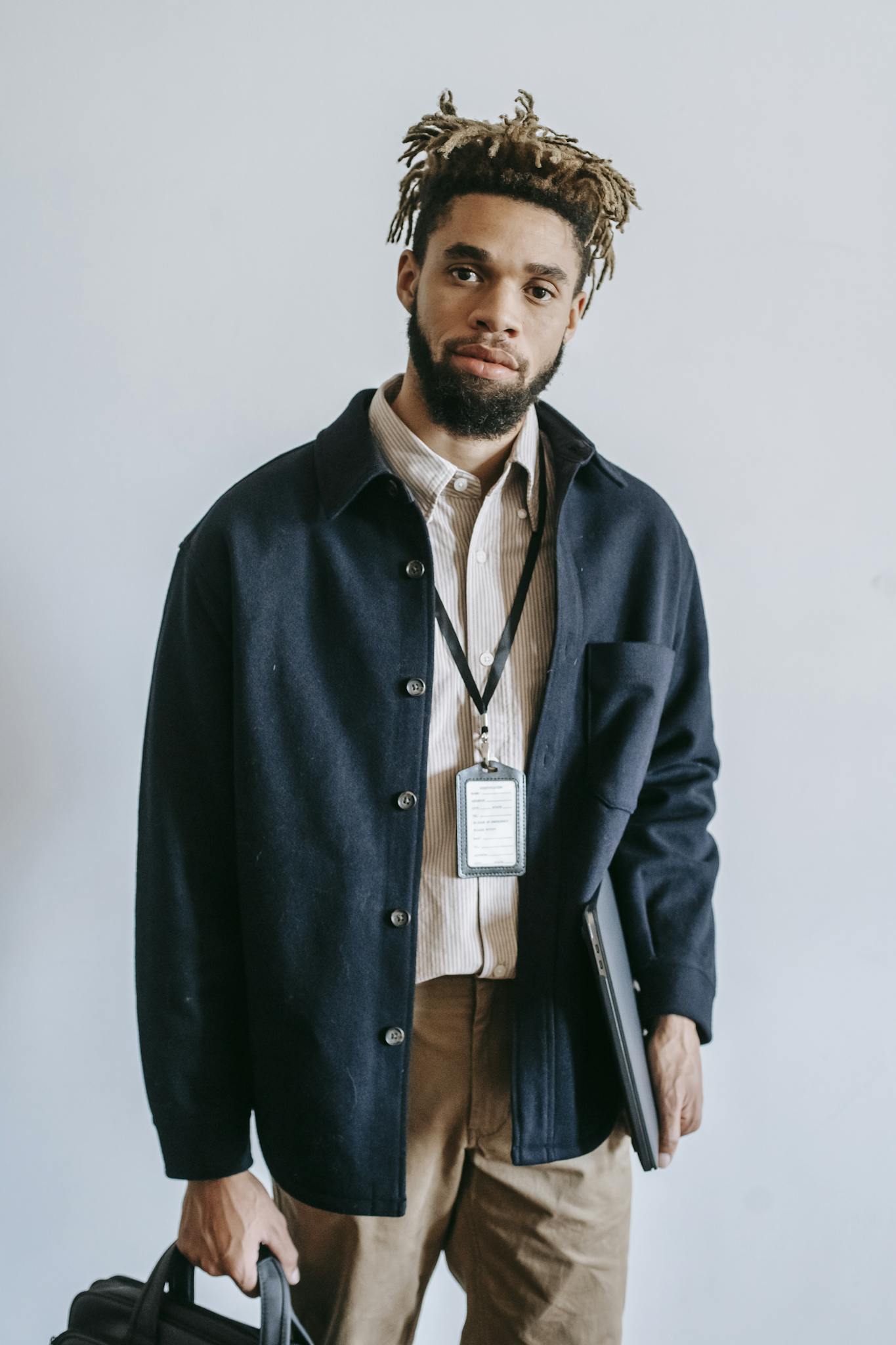 Portrait of a confident young African American man with laptop and bag, standing indoors.